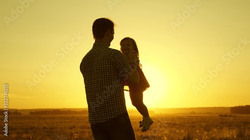 Dad beloved child in her arms dances in flight and laughs. Happy baby plays with his father at sunset. Silhouette of a man and a child. Family concept.