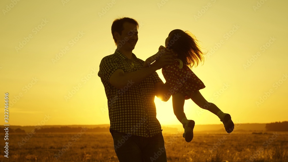 Dad beloved child in her arms dances in flight and laughs. Happy baby plays with his father at sunset. Silhouette of a man and a child. Family concept.