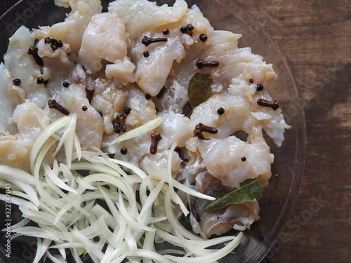 XE salad of freshly salted river pike fish on a cutting kitchen board with ingredients for cooking. Pike fillet pieces. Wooden brown background.