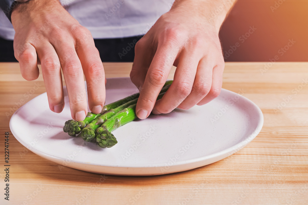 Man laying out steamed green asparagus on the plate, preparing food presentation Man laying out steamed green asparagus on the plate, preparing food presentation