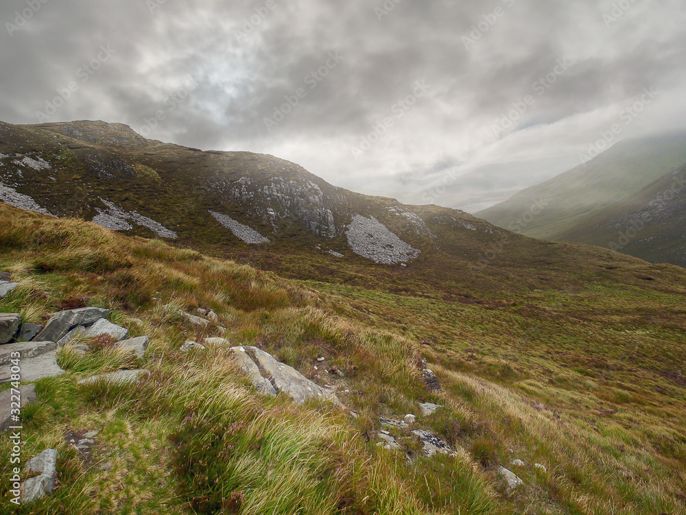 Mountains in Connemara, county Galway, Stone patches in grass land, Cloudy sky. Nobody.