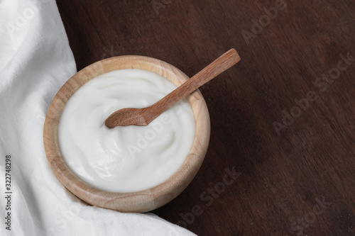 Natural homemade plain organic yogurt in wooden bowl and wood spoon on wood texture background