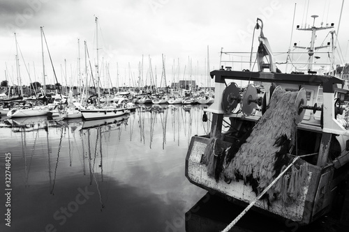 Fishing ship and sailing boats at harbor in cloudy day. Normandy  France. Fishing industry and leisure sailing tourism concept. Nautical background. Black white photo.