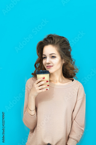 Portrait of a young beautiful woman wearing sweatshirt holding a cup with hot drink in hands over blue background