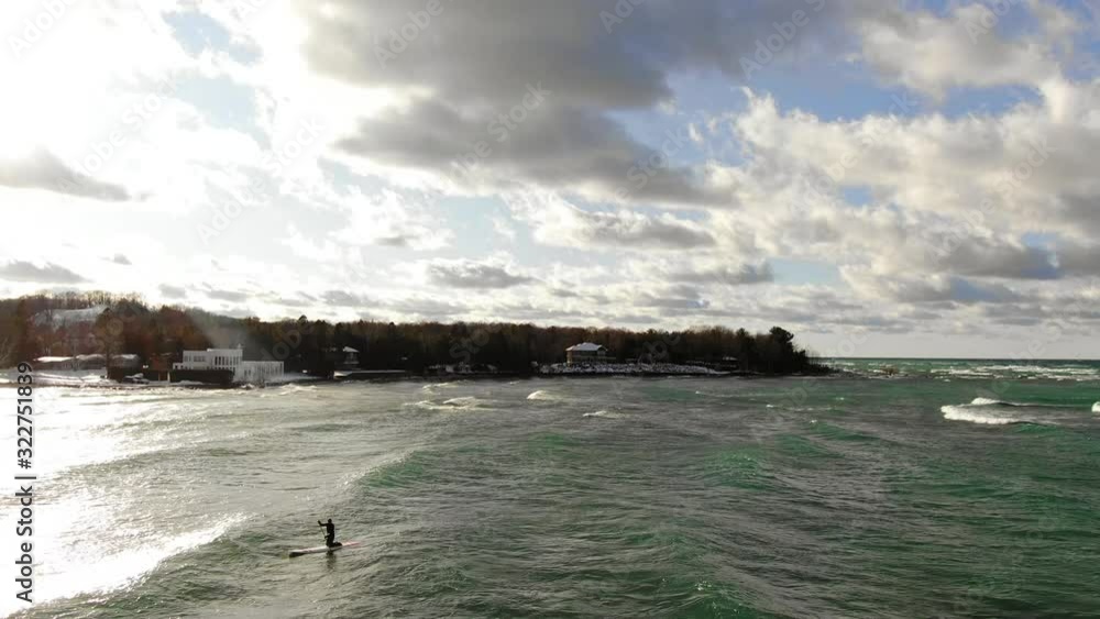 Winter stand up paddle surfing in Northern Michigan Charlevoix Petoskey Area on Lake Michigan sun flare with surfer at winter beach inland surfing Winter stand up paddle surfing in Northern Michigan Charlevoix Petoskey Area on Lake Michigan sun flare with surfer at winter beach inland surfing