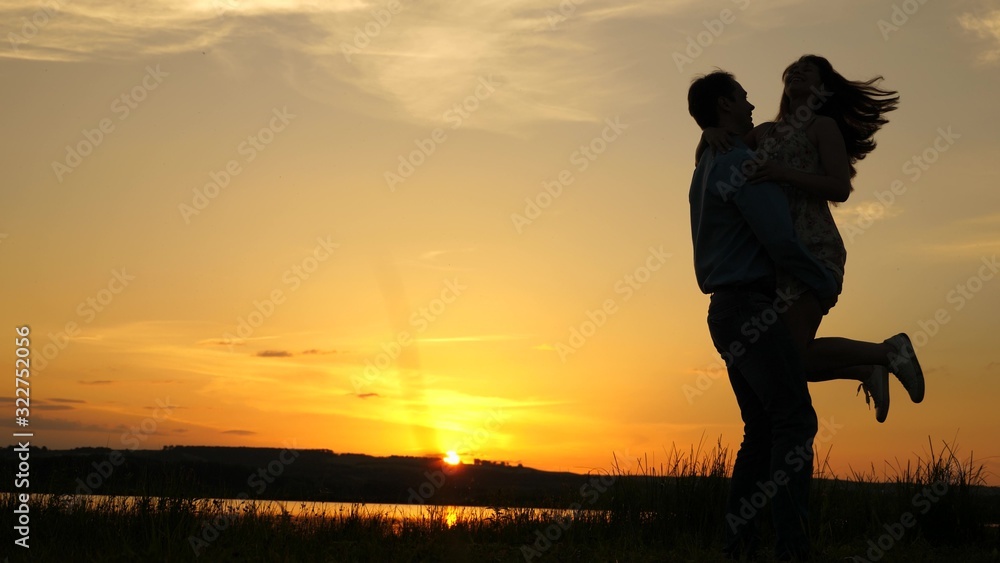 Young couple dancing at sunset on beach. Happy guy and girl waltz in evening in summer park. Loving man and woman dance in bright rays of sun on the background of the lake.