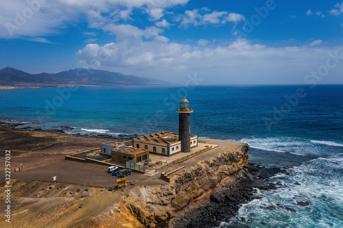 Reflexes on the water puddles of cliffs and lighthouse, Jandia tip in coast of Fuerteventura, Canary islands. Aerial drone shot, october 2019