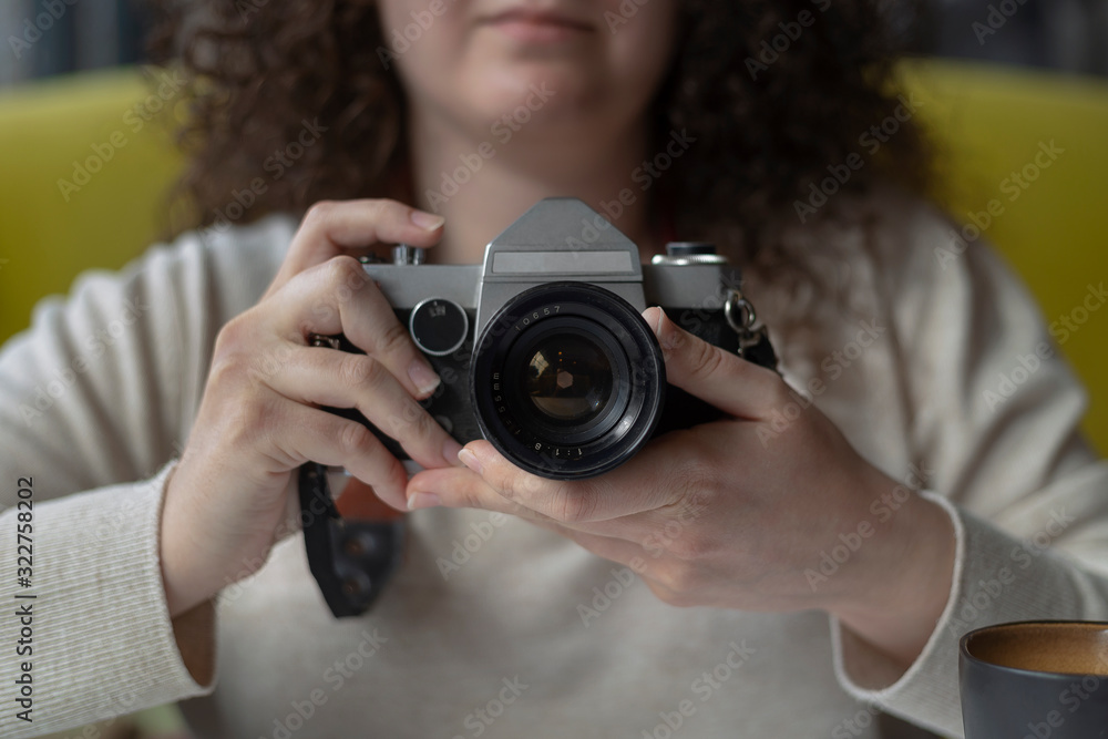 Curly haired photographer woman holding her camera in a cafe and shooting Curly haired photographer woman holding her camera in a cafe and shooting