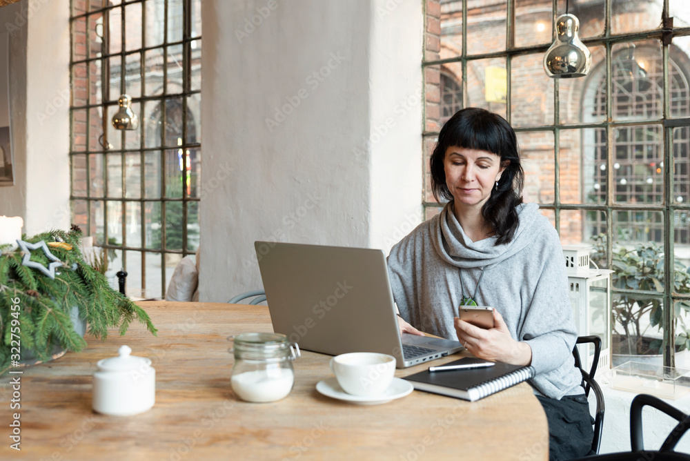 businesswoman working on laptop at cafe with industrial window. She is holding the phone and has a cup of coffee. Freelancer. businesswoman working on laptop at cafe with industrial window. She is holding the phone and has a cup of coffee. Freelancer.