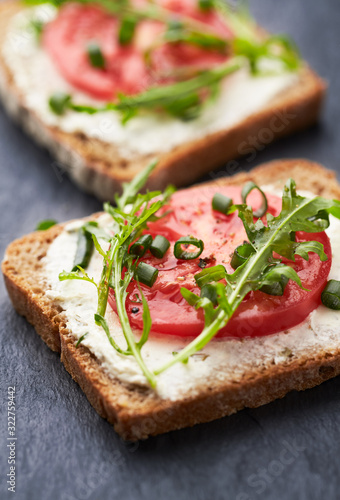 Healthy Breakfast Idea. Tomato sandwich with cream cheese and fresh rocket on black stone background. Close up. 