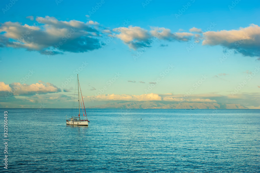 A small boat bobs on the surface of a calm sea. Dawn over the ocean. Colorful sky and calm ocean. An island is visible in the distance.