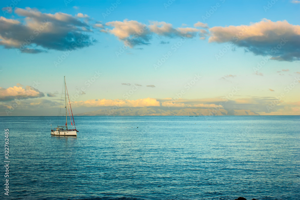 A small boat bobs on the surface of a calm sea. Dawn over the ocean. Colorful sky and calm ocean. An island is visible in the distance.