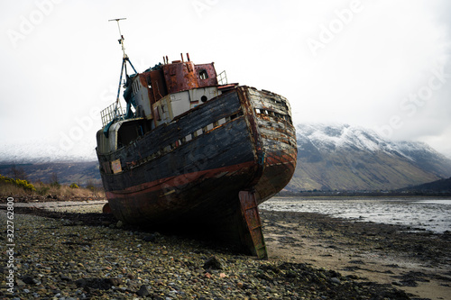 Wrecked wooden fishing boat on beach near Corpach village, Fort William, Scotland, United Kingdom. Broken abandoned boat in sand of sea bay. Wheatered wood and rusty meatal part photo