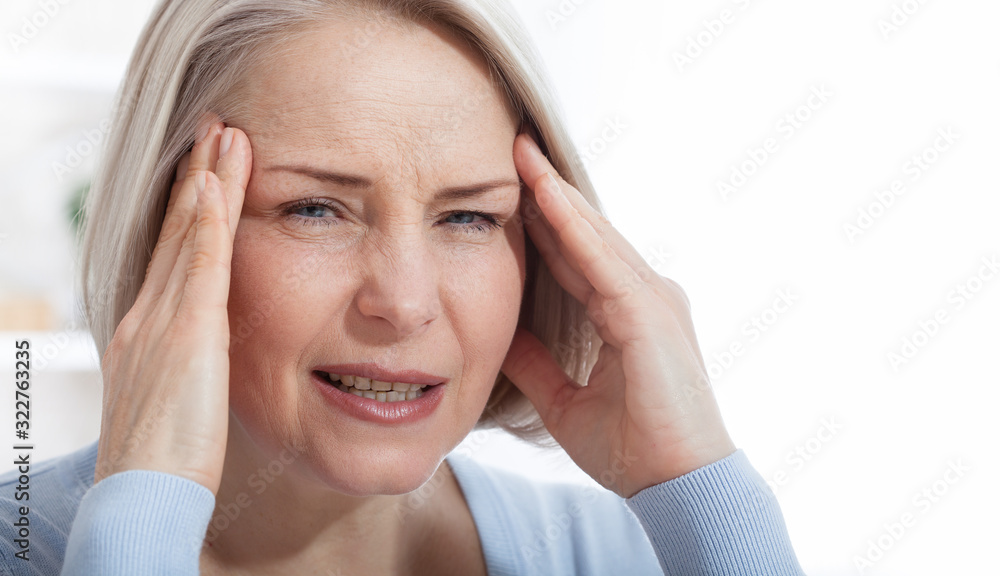 Woman suffering from stress or a headache grimacing in pain as she holds the back of her neck with her other hand to her temple, with copyspace. Concept photo with indicating location of pain. Woman suffering from stress or a headache grimacing in pain as she holds the back of her neck with her other hand to her temple, with copyspace. Concept photo with indicating location of pain.