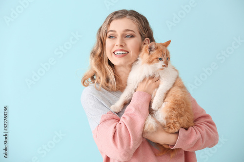 Beautiful young woman with cute cat on color background