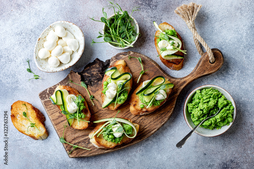 Appetizer crostini with mashed green pea, mozzarella, pea sprouts and zucchini ribbons on wooden board. Delicious healthy snack, spring appetizers