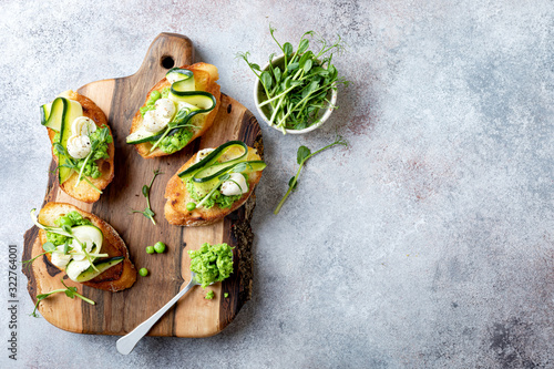 Konstfotografi Appetizer crostini with mashed green pea, mozzarella, pea sprouts and zucchini ribbons on wooden board