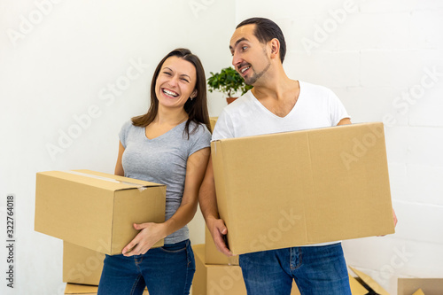 Happy couple looking at camera, holding boxes, ready to move into their new house.