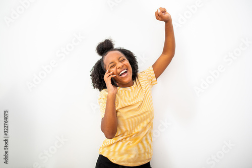 cheerful african american girl talking with mobile phone and arm raised by white background