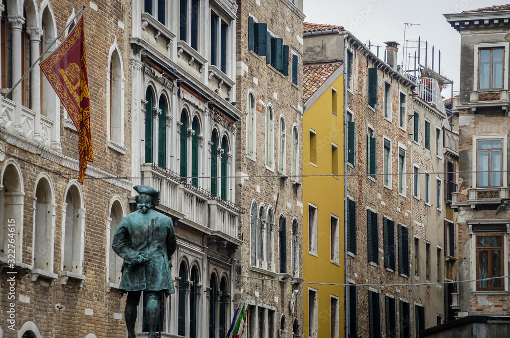Sculpture in Venice with street and colored buildings. Italy, Europe.