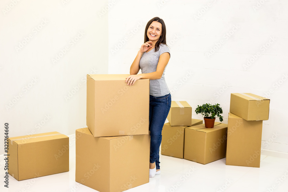 Happy woman prepared all carton boxes for moving into new flat and stands leaning on a pile of boxes, smiling to the camera. Happy woman prepared all carton boxes for moving into new flat and stands leaning on a pile of boxes, smiling to the camera.