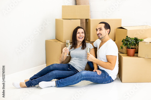 Young couple celebrating, sitting among boxes, drinking champange and plannig how they will furnish their new house. © Andrii