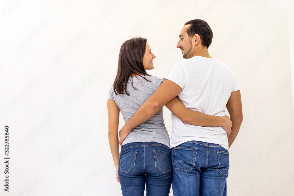 Back view of young couple standing together, embracing, looking at white wall. Back view of young couple standing together, embracing, looking at white wall.