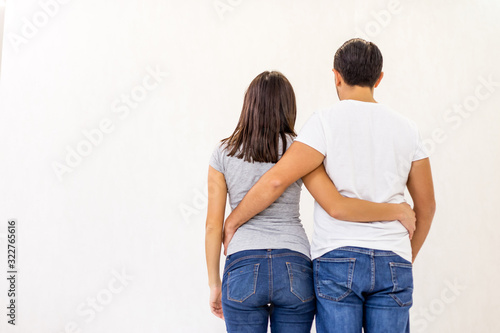 Back view of young couple standing together, embracing, looking at white wall.