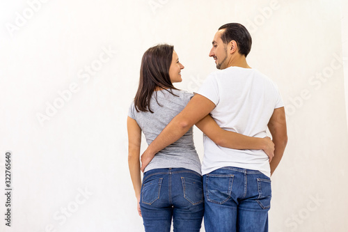 Back view of young couple standing together, embracing, looking at white wall. © Andrii
