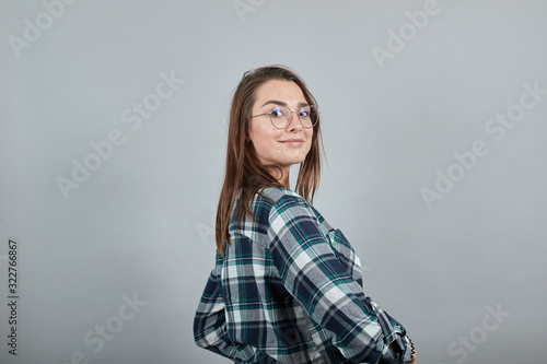 Young brunette girl blue green in checked shirt on grey background happy woman turned sideways smiles, demonstrates peleche