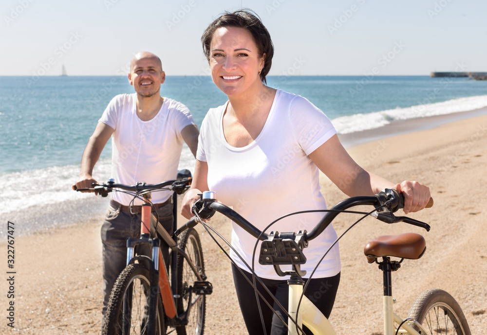 mature man and female walking with bicycles along the sea