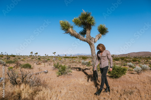 Joshua tree a curly haired blonde man is walking in the fierce heat and deep blue skies of the south western desert of North America, wearing dark sunglasses, a beige linen shirt