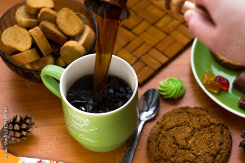 Coffee is poured from Turki into a mug. A woman's hand holds a Turk and pours strong coffee into a green mugCoffee is poured from Turki into a mug. A woman's hand holds a Turk and pours strong coffee  photo