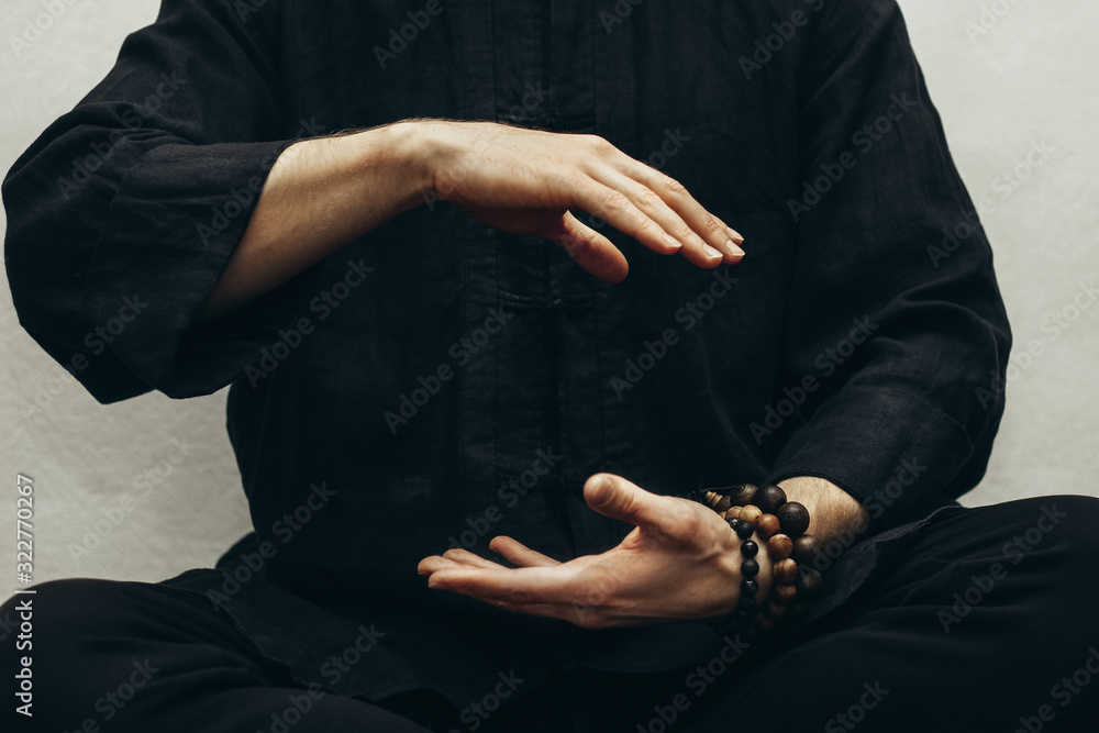 A man in black shirt sitting and doing qigong. Hands direct energy. Prayer, gratitude.Practicing monk. Qi energy. Yoga pose. Close up