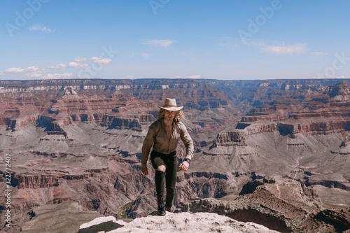 A Curly haired blonde man, wearing a beige T-Shirt ,black jeans, black shoes, beige linen shirt and matching cowboy hat, background vistas of the Grand Canyon