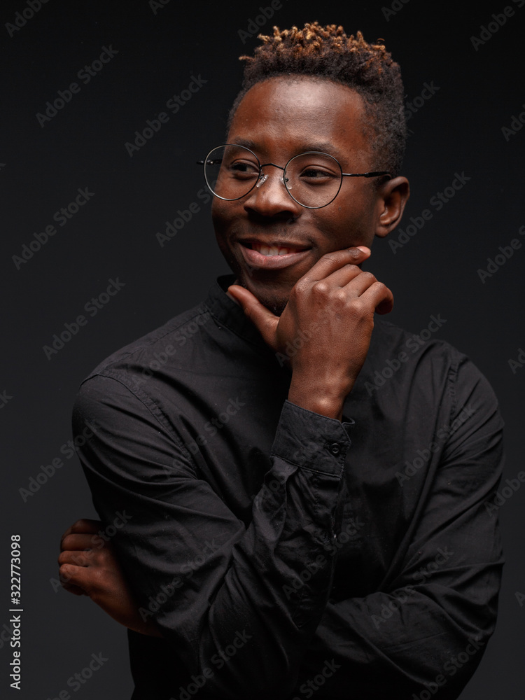 Fototapeta premium Emotional portrait of a young African man in black clothing against a dark background. Studio photography.
