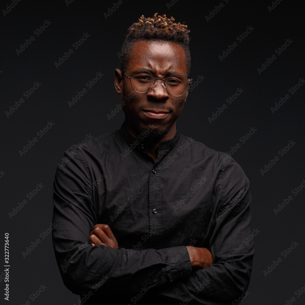 Emotional portrait of a young African man in black clothing against a dark background. Studio photography.