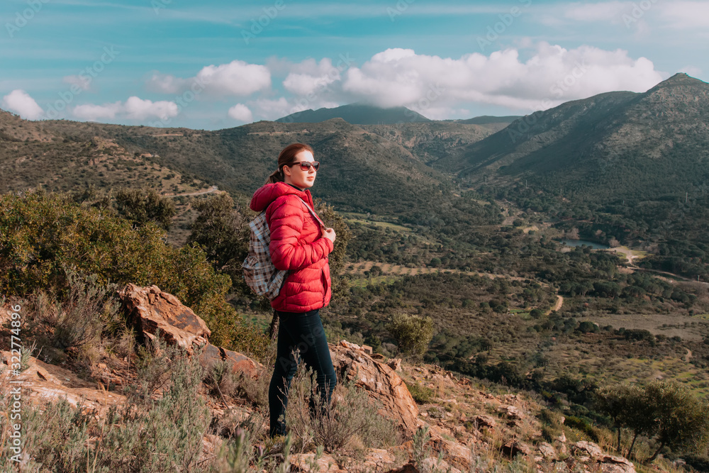 Fototapeta premium Young woman enjoying view on mountains in sunset, beautiful nature scenery with mountain tops. Girl or woman traveler with backpack alone, woman travelling solo, view from behind, vacation concept