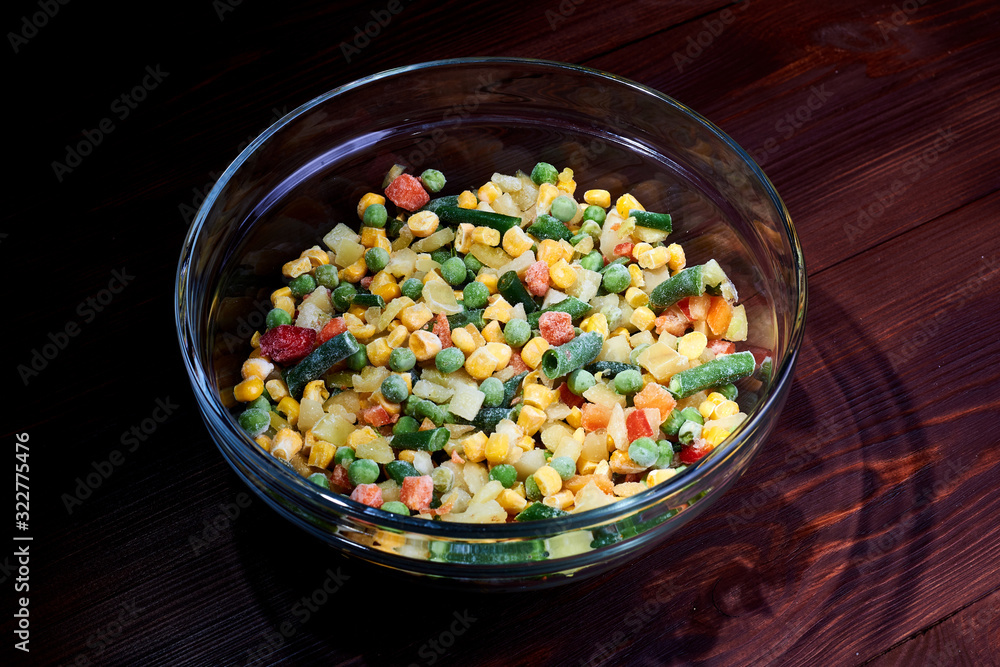 Frozen different vegetables in a glass plate on a wooden background. Frozen different vegetables in a glass plate on a wooden background.