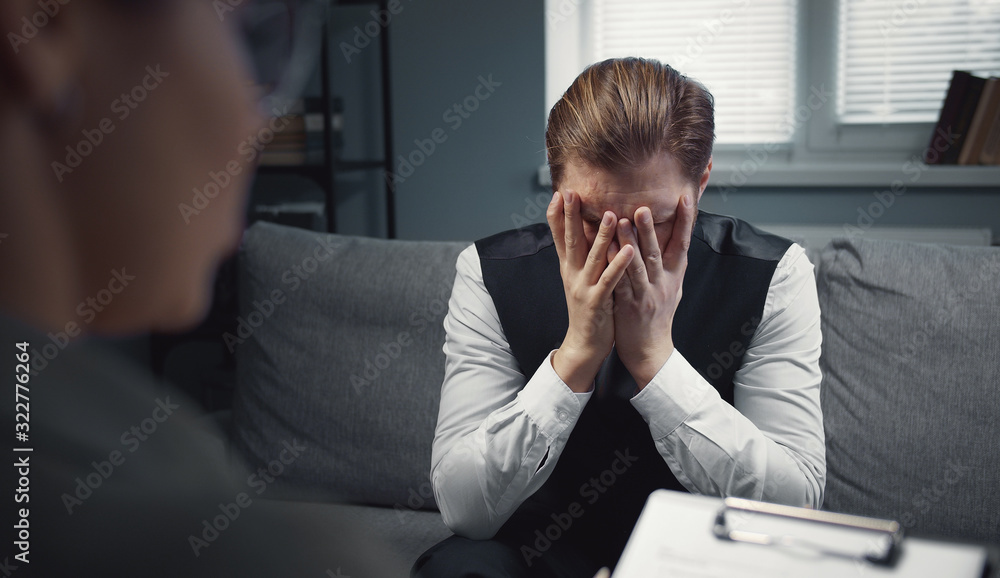 Depressed male client talking to female psychiatrist about his issues closing his face with hands Depressed male client talking to female psychiatrist about his issues closing his face with hands