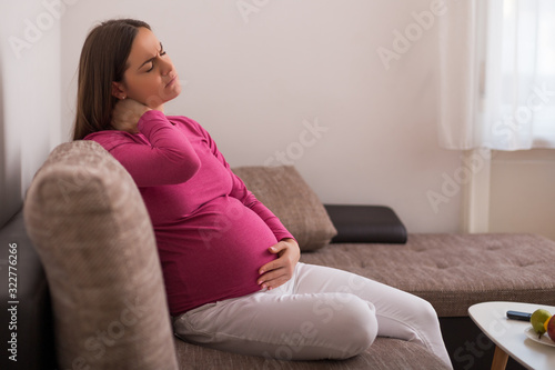 Pregnant woman having neck pain while spending time at her home.