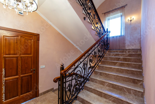Stairs in the cottage with wrought iron railings and wooden handrails. Marble steps. 