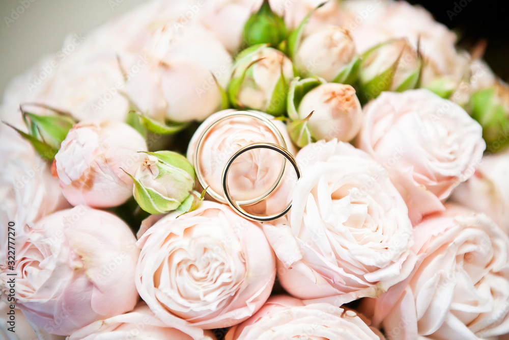 Bride wedding bouquet. Golden rings on top of pink roses background. Ceremony jewelry symbol of love.