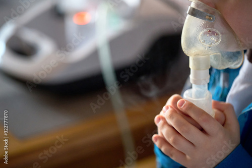 Child makes inhalation at home with nebulizer on out of focus background. Example of combating respiratory diseases such as tracheitis bronchitis pneumonia with medical equipment at home conditions