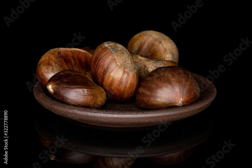 Group of six whole edible brown chestnut with brown ceramic coaster isolated on black glass photo