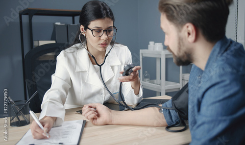 Woman physician measuring patient's blood pressure and writing it down to medical record