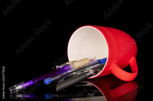 Lot of whole writing ballpoint pen with red ceramic cup isolated on black glass