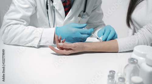 Close-up of doctor's hands in blue latex gloves making injection to female patient's forearm photo