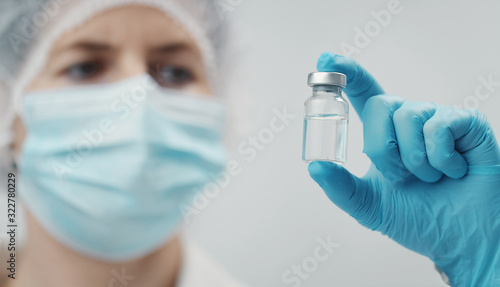 Closeup of medical doctor holding vaccine in transparent glass vial between fingers, focus on bottle
