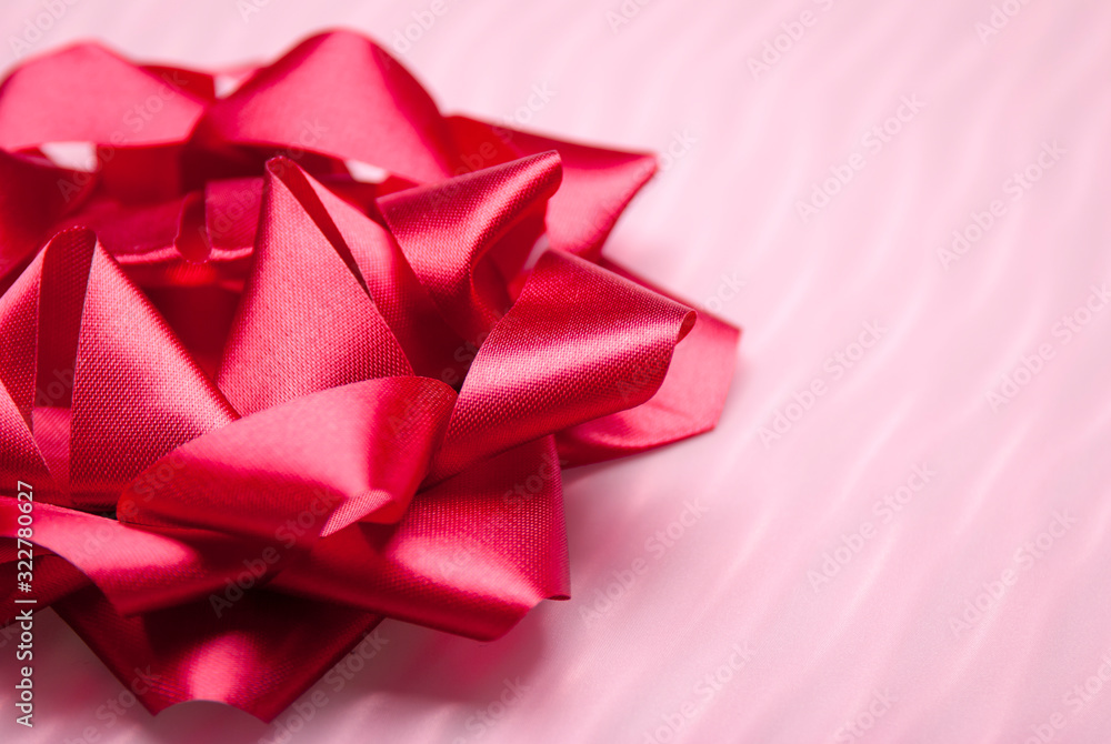 Shiny red bow sitting on textured pink background Shiny red bow sitting on textured pink background
